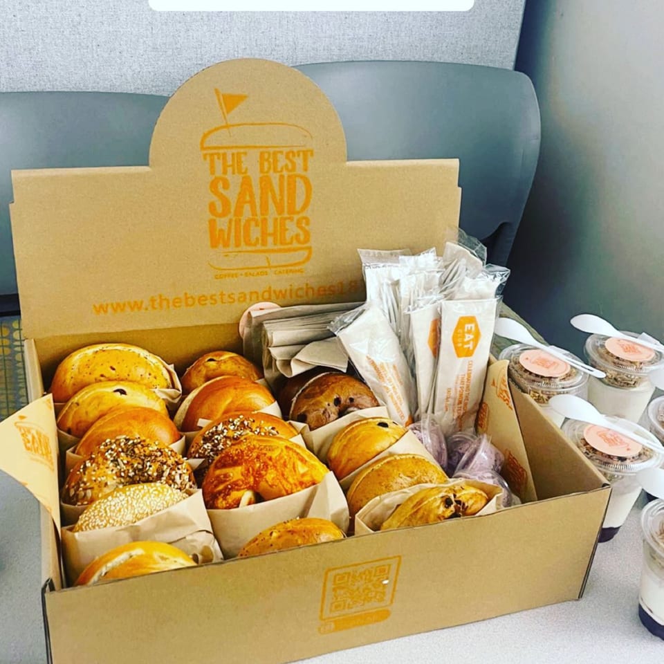 A catering box from The Best Sandwiches filled with bagels, utensils, and yogurt parfaits.