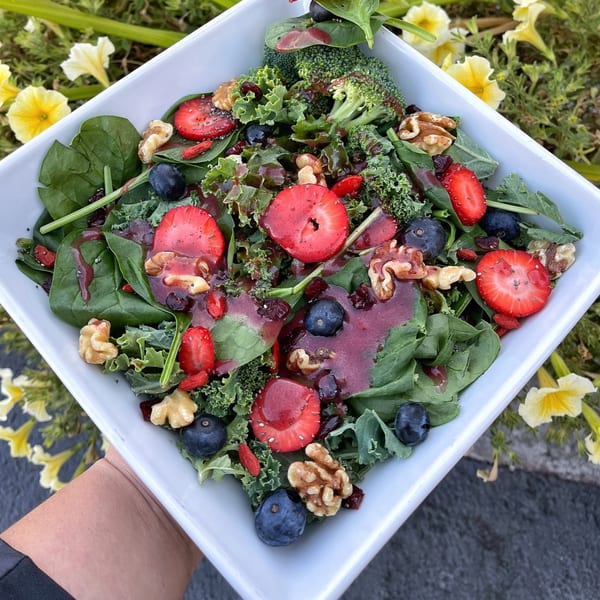 A vibrant salad with spinach, kale, strawberries, blueberries, walnuts, and a berry vinaigrette.