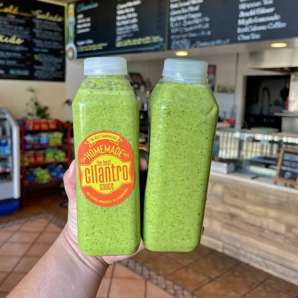 Two bottles of The Best Sandwiches' homemade cilantro sauce held in a restaurant setting.