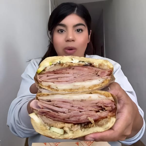 A woman holds up a large, sliced sandwich overflowing with deli meats and cheese.